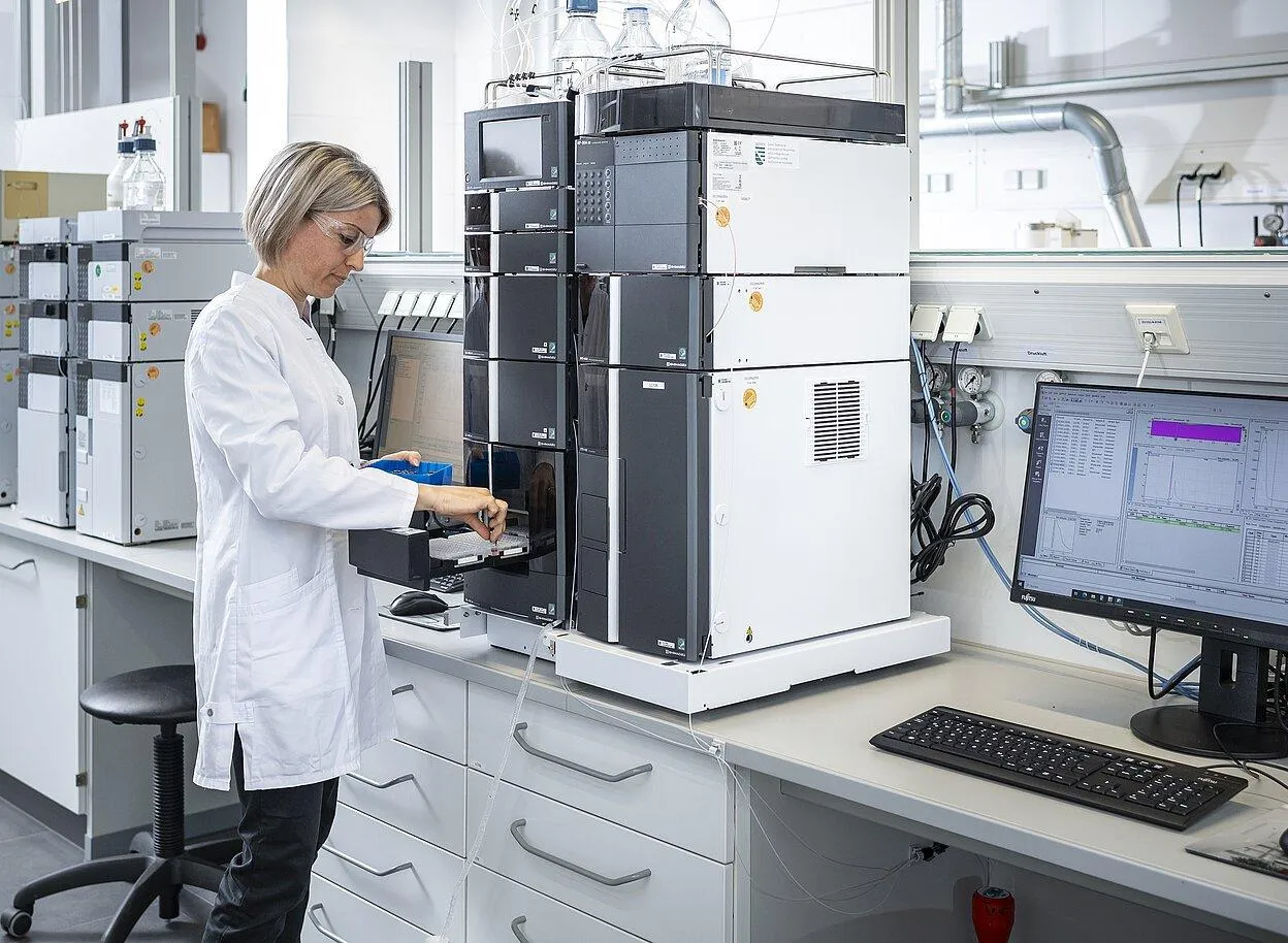 Female laboratory technician operating analytical equipment beside a computer displaying measurement data